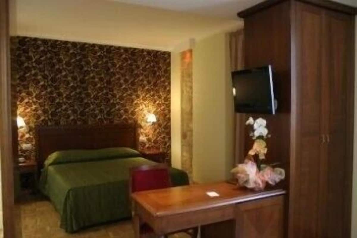 A hotel room with a bed, a desk, a television, and a wall with a patterned design.