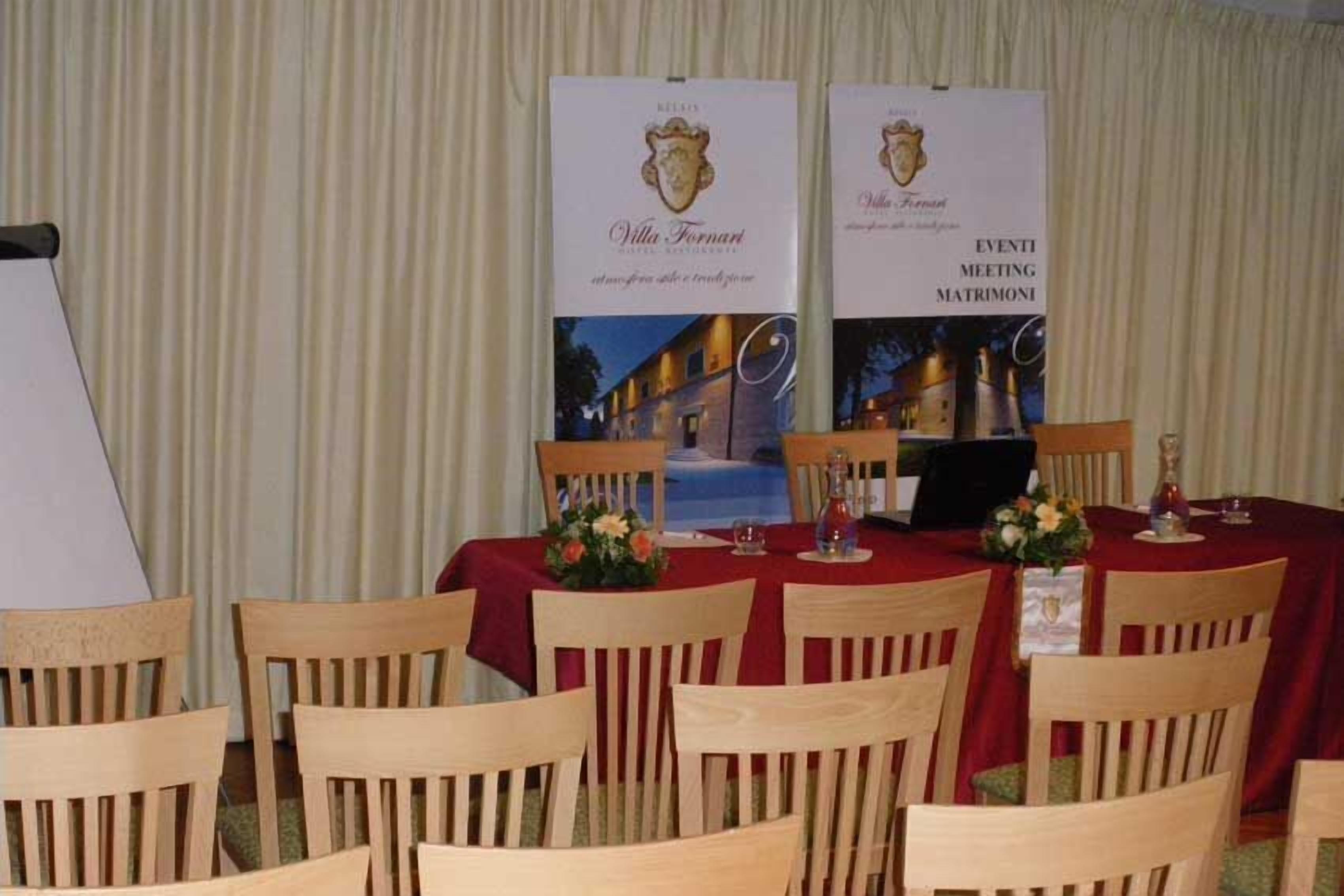 Une salle de banquet avec des chaises et des tables en bois, des bannières aux couleurs de Villa Tornan et de Villa Ferna, et un écran de projection.