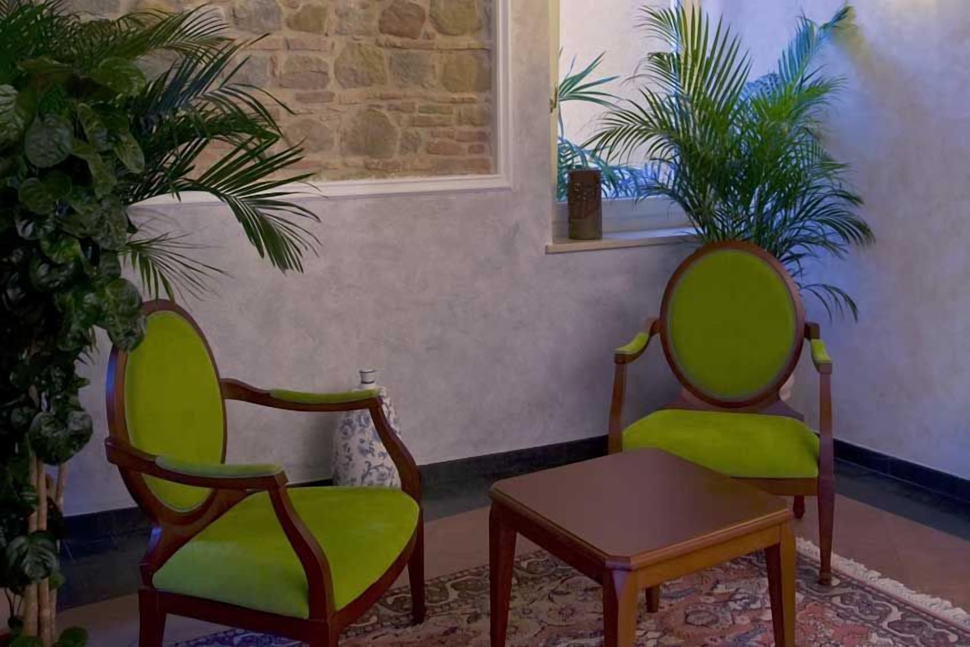 A room with two green upholstered chairs, a wooden table, and a stone wall.
