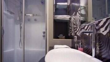 A bathroom with a glass shower enclosure, a white sink, and zebra-striped towels.