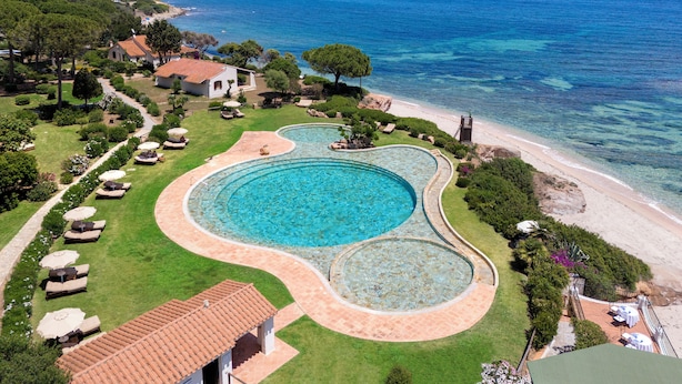An aerial view of a resort with a large swimming pool, a beach, and ocean views.