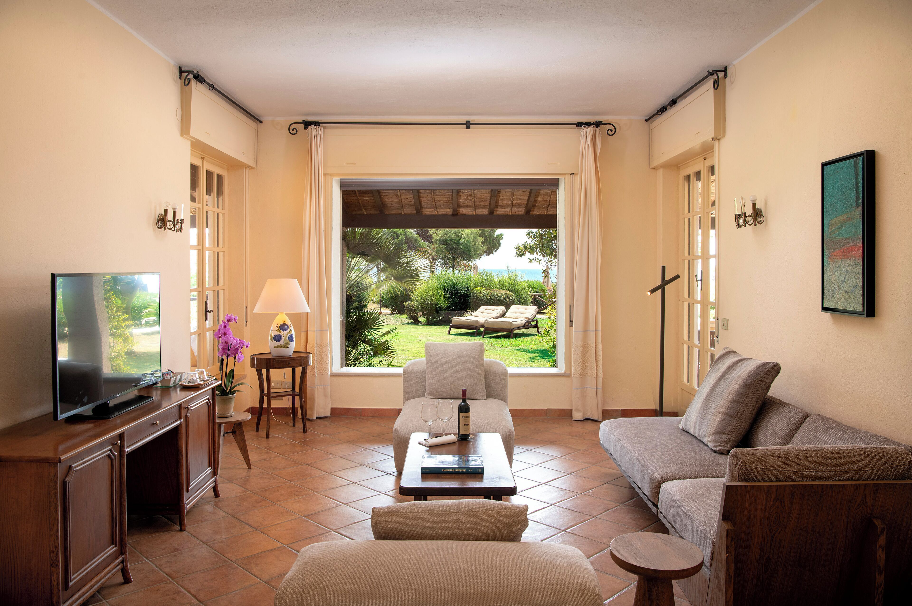 A living room with a TV, sofa, coffee table, and a view of a garden.