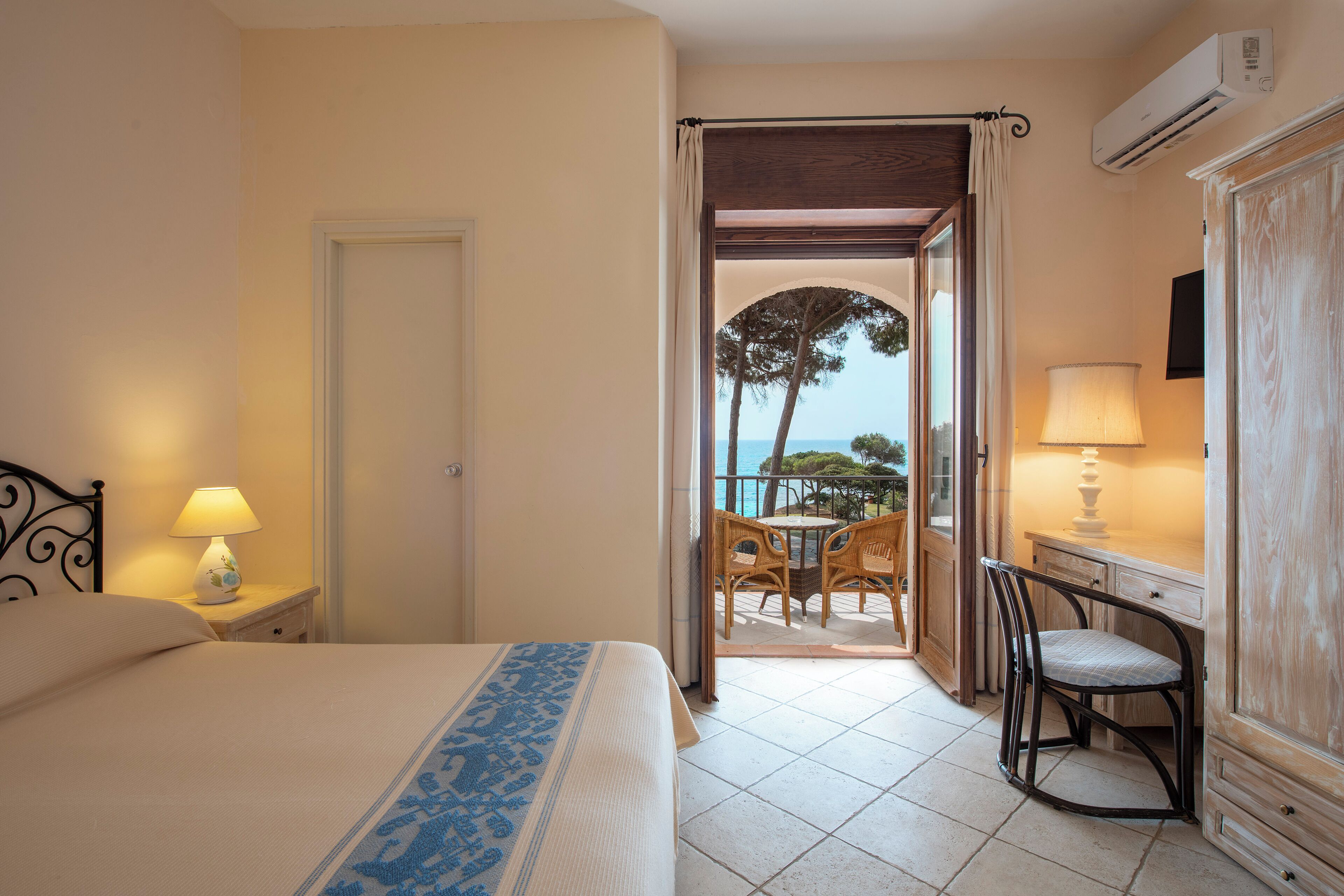 Habitación de hotel con cama, mesita de noche con lámpara, una silla, una mesa y un aire acondicionado.