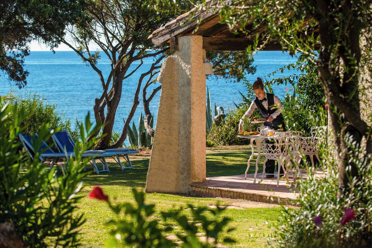 Un jardín con un pilar de piedra, una mesa con sillas y vistas al mar.