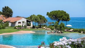 A swimming pool with a curved edge, surrounded by a grassy area and a white building with a tiled roof.