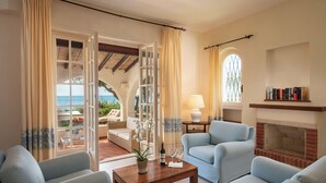 A living room with a sofa, armchairs, a coffee table, and a fireplace. There is a view of the outdoors through a glass door.