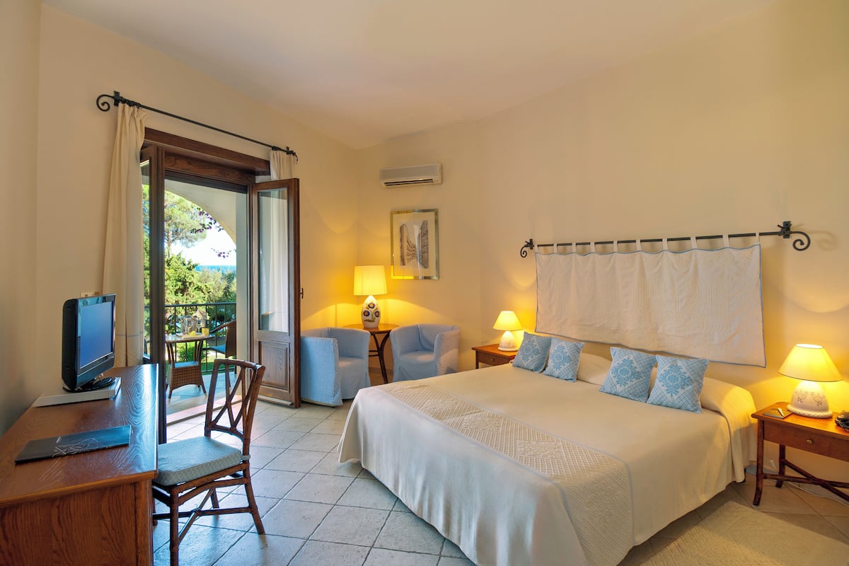 Habitación de hotel con cama, dos sillas, escritorio con computadora y televisión.