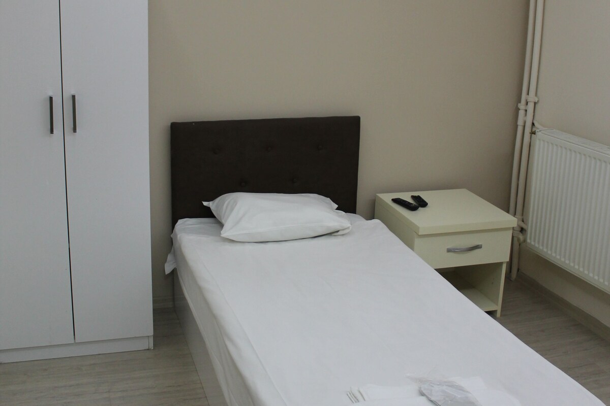 A neatly made bed with white linens, a bedside table with a remote control, and a wardrobe with two doors.