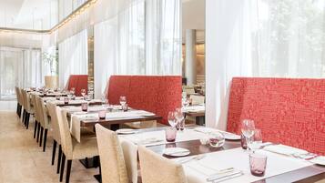 Een restaurant met lange tafels, rode, beklede zitbanken en een lichte, ruimtelijke sfeer.