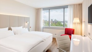 Habitación de hotel con una cama grande, un escritorio, una silla, un televisor y una ventana con vista a la ciudad.