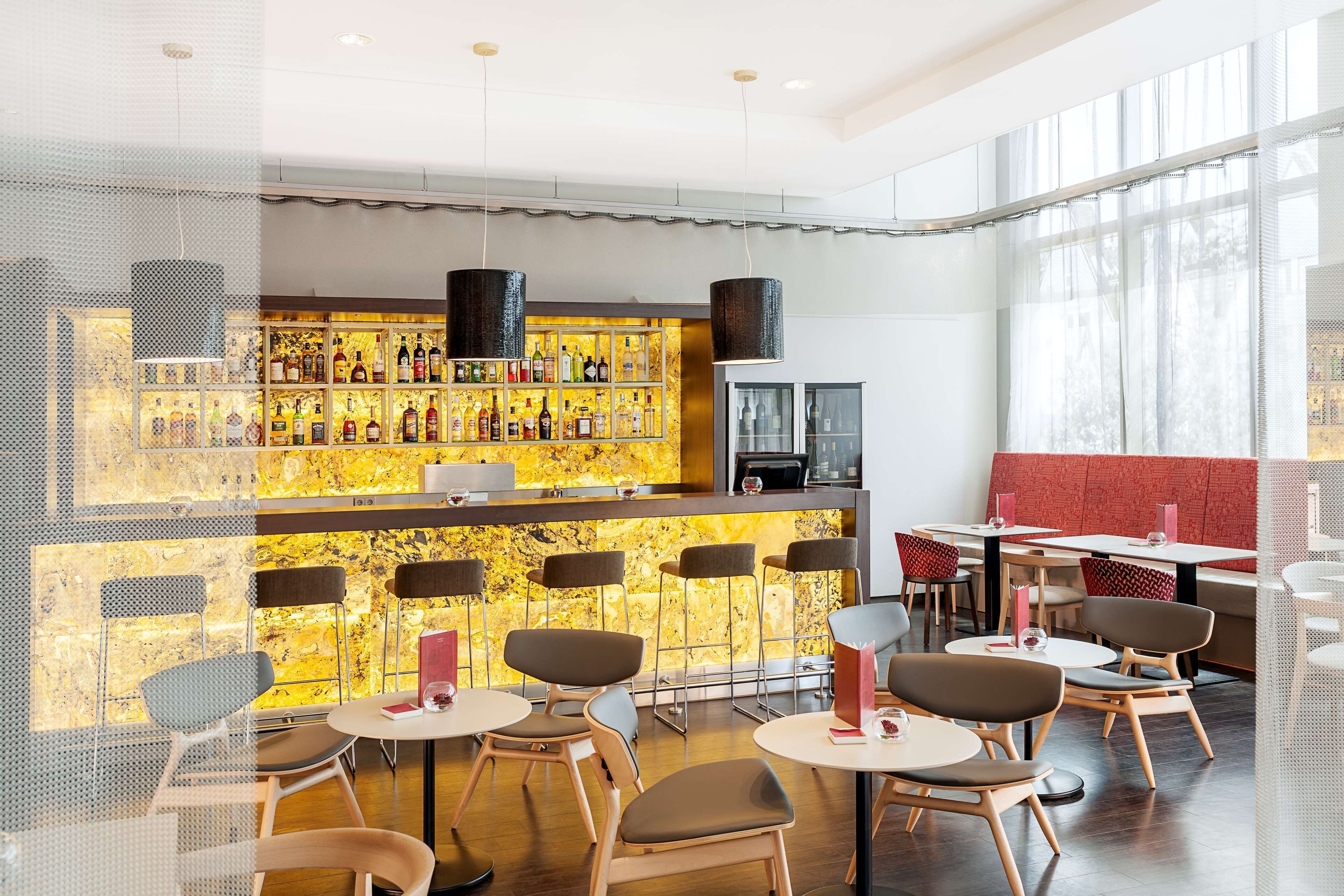 Un espace bar moderne doté d’un comptoir en marbre, de plusieurs options d’assises et d’une grande fenêtre laissant entrer la lumière naturelle.