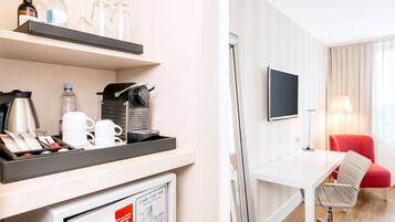 Ein Hotelzimmer mit Schreibtisch, Fernseher, einem roten Sessel und einer Minibar mit verschiedenen Artikeln.
