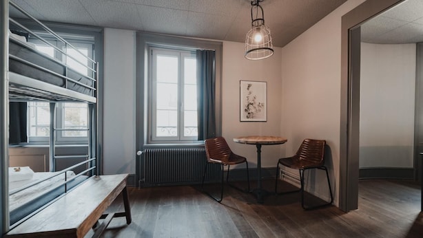 A room with a bunk bed, a round table with chairs, a radiator, and a hanging light fixture. - Falken Hotel & Backpacker (Interlaken)