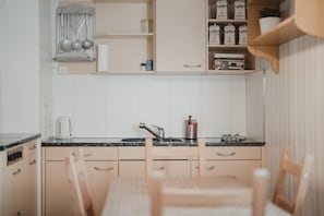 Una cocina con armarios blancos, un lavamanos, una cafetera y una estantería con frascos.