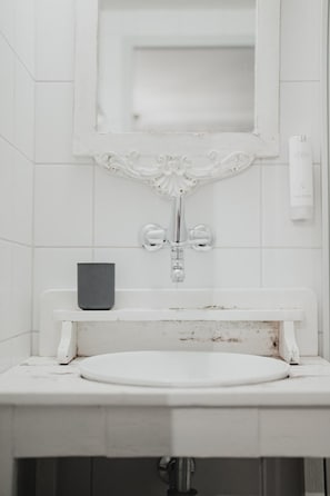 Un baño con un lavamanos blanco, un espejo encima y un pequeño objeto negro en la encimera.