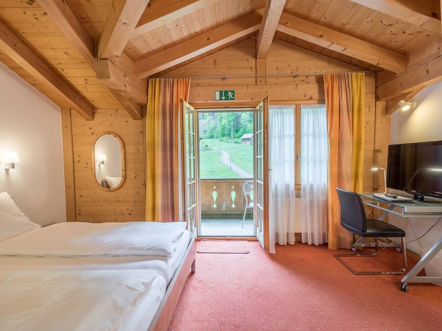 Habitación de hotel con cama, escritorio con computadora, televisor y vista al exterior.