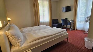 Habitación de hotel con cama, escritorio, silla, televisor y ventana con cortinas.