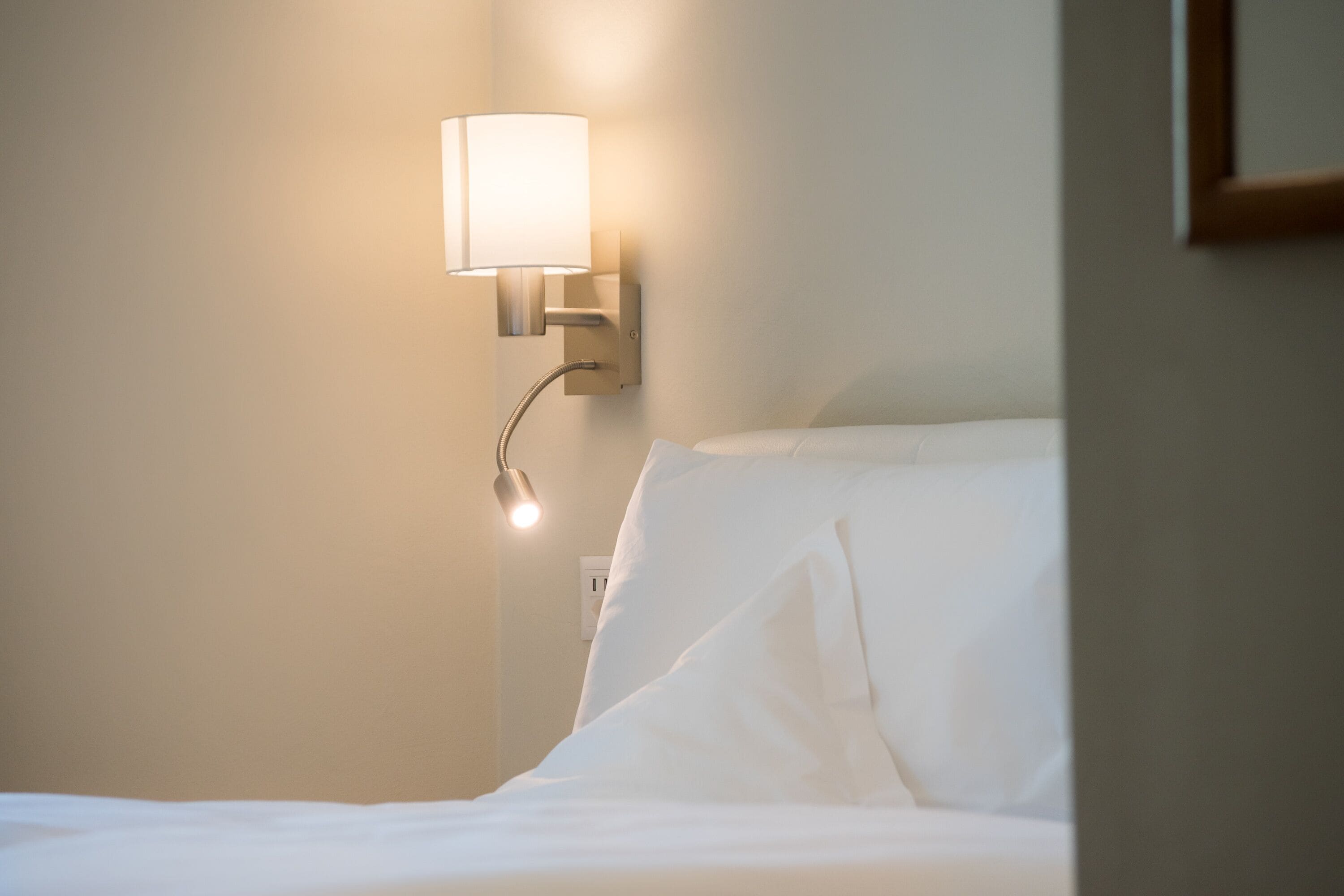 Habitació d'hotel amb un llit, una làmpada penjada a la paret i una presa elèctrica visible.