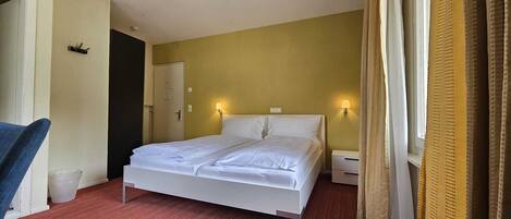 Une chambre d’hôtel avec un lit, une chaise, une table de chevet et une porte.