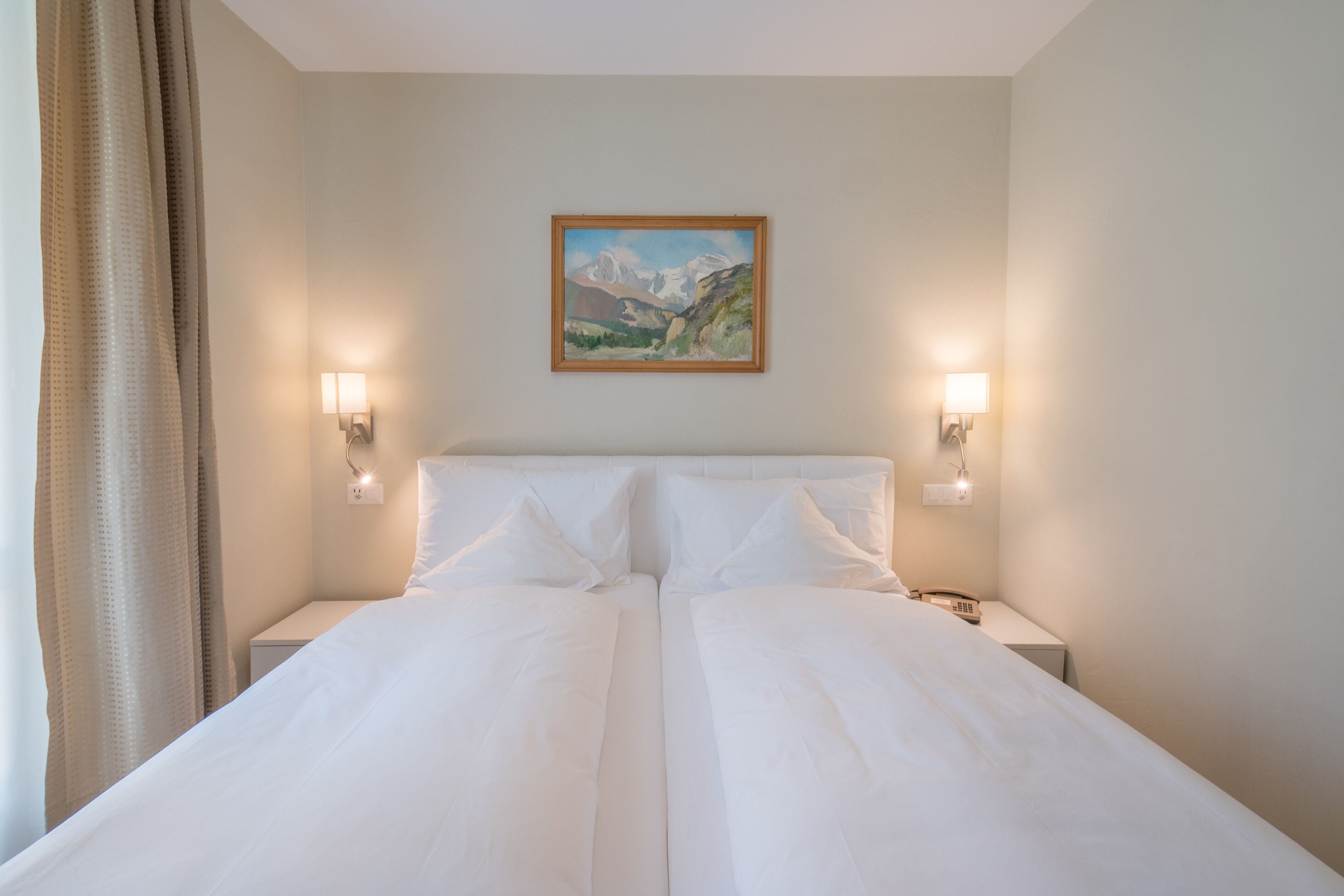 Ein Doppelbett mit weißer Bettwäsche, zwei Nachttische mit Lampen und ein Gemälde einer Berglandschaft an der Wand.