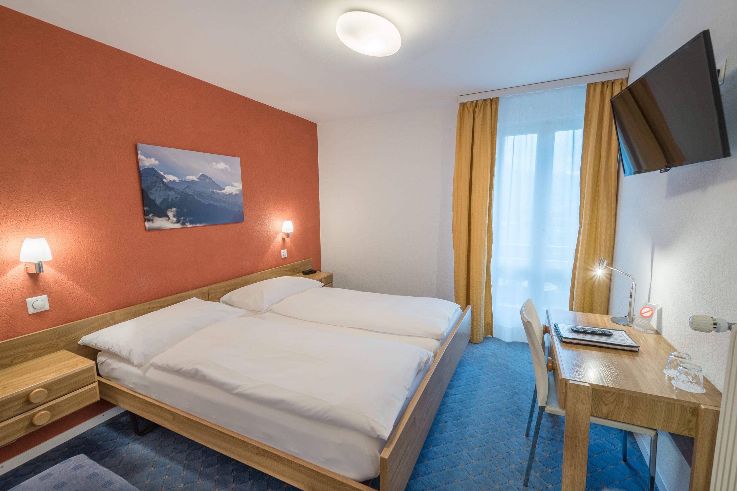A hotel room with two beds, a desk, a chair, a TV, and a painting on the wall.