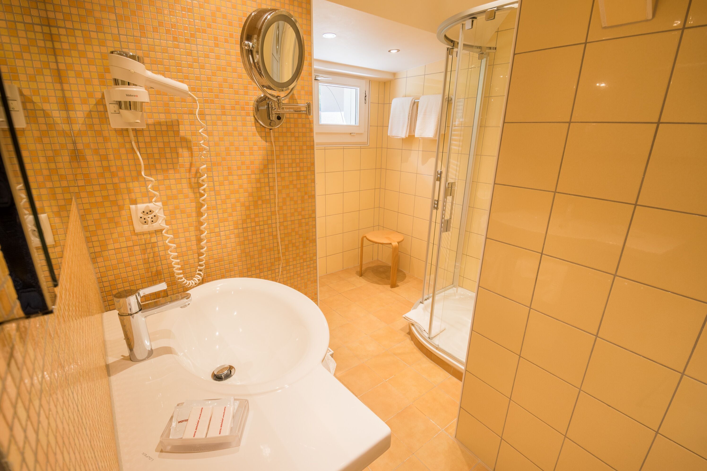 A bathroom with a sink, mirror, hairdryer, and a glass shower enclosure.
