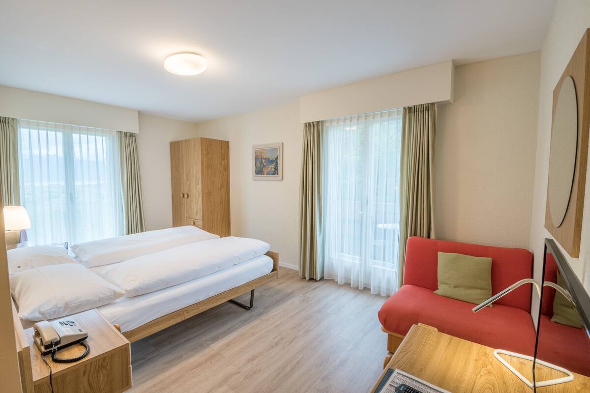 Habitació d'hotel amb un llit, un sofà vermell, una petita taula de nit de fusta amb un telèfon i un mirall.