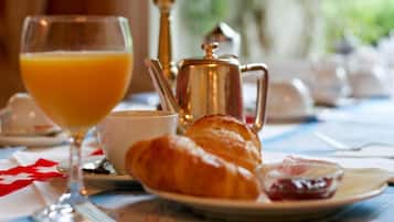 Desayuno con cruasanes, un vaso de jugo de naranja y una cafetera sobre una mesa.