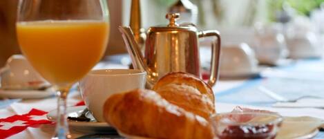 A breakfast setting with croissants, a glass of orange juice, and a coffee pot on a table.