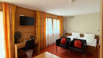 A hotel room with a bed, a desk, a chair, a small table, and a TV mounted on the wall.