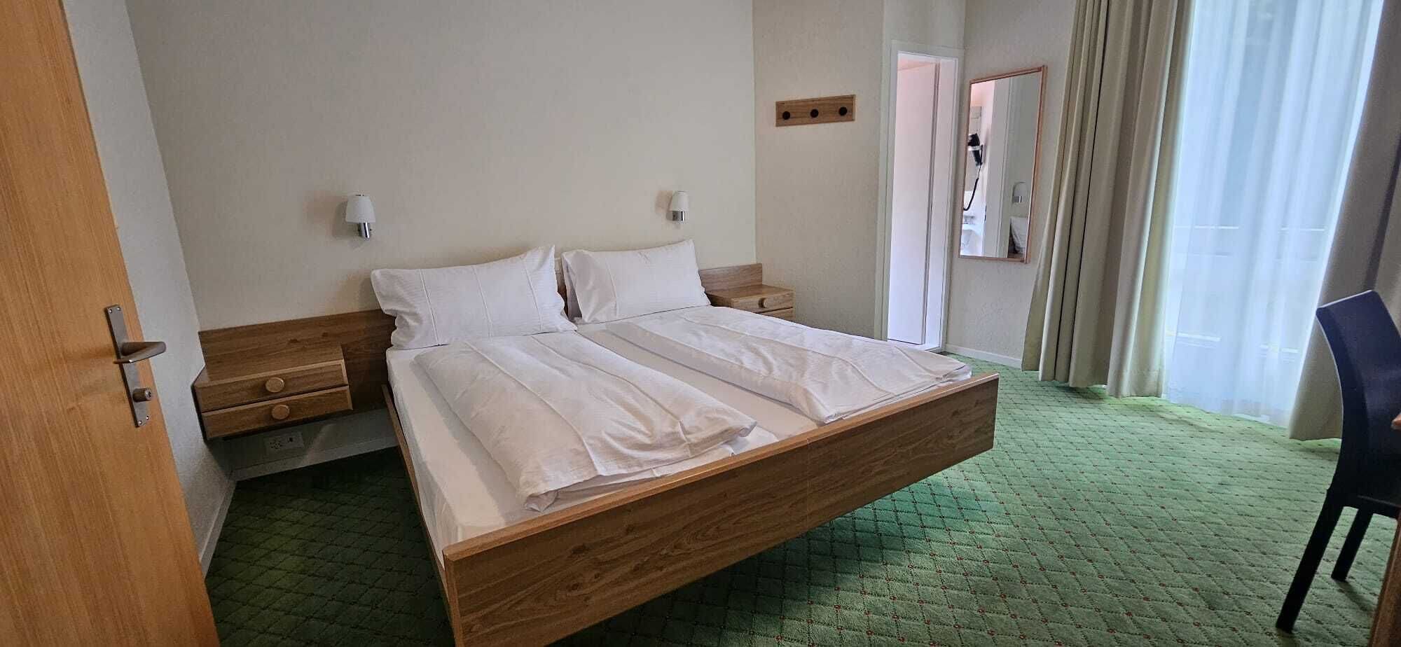 Een hotelkamer met een houten bed, twee nachtkastjes, een spiegel en een groen tapijt.