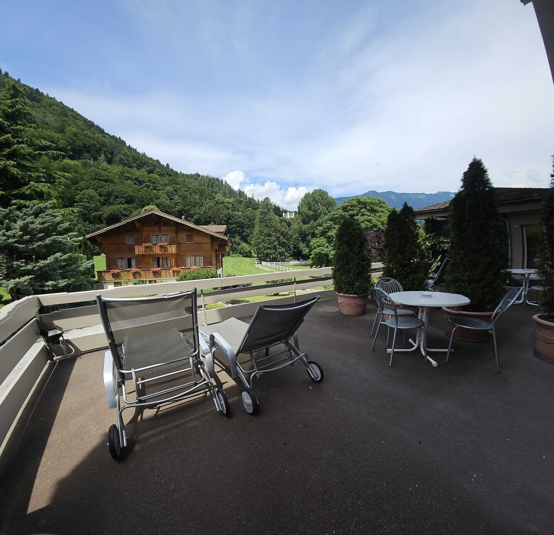 Eine Terrassesituation mit Blick auf einen Berg, ein Holzgebäude und ein Essbereich mit Stühlen und Tisch.