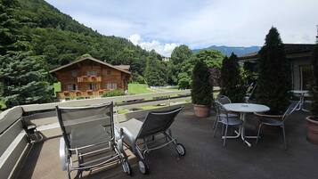 Eine Terrassesituation mit Blick auf einen Berg, ein Holzgebäude und ein Essbereich mit Stühlen und Tisch.