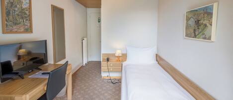 Una habitación de hotel con un escritorio de madera, una cama y dos cuadros en las paredes.