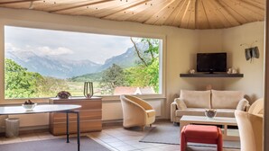 Un salon moderne doté d’une grande fenêtre offrant une vue sur les montagnes, d’un téléviseur à écran plat et d’un coin salon confortable.