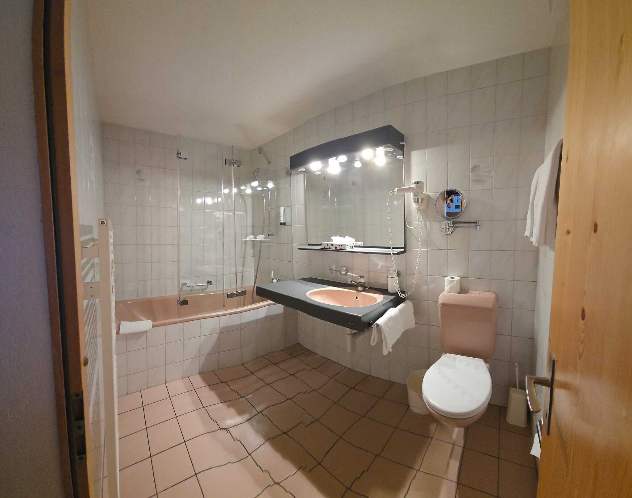 A bathroom with a bathtub, sink, toilet, and a mirror with lights.