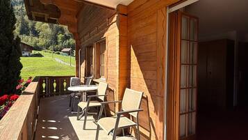 A wooden building with a covered outdoor area, a table with chairs, and a view of a green landscape.