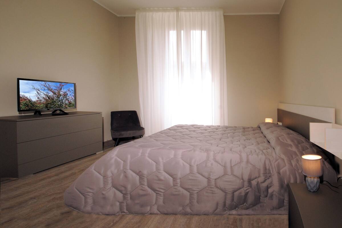 A bedroom with a bed, a dresser, a chair, and a TV on a dresser.