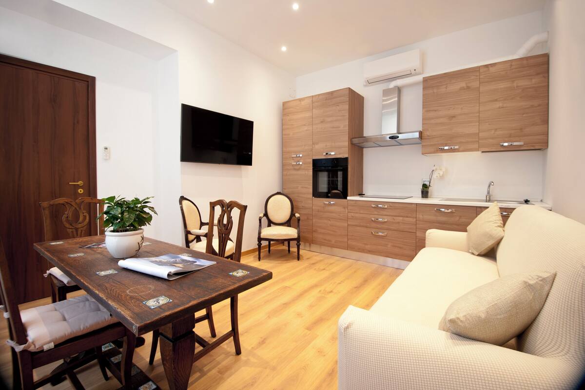 A modern kitchen with wooden cabinets, a built-in oven, and a flat-screen TV.