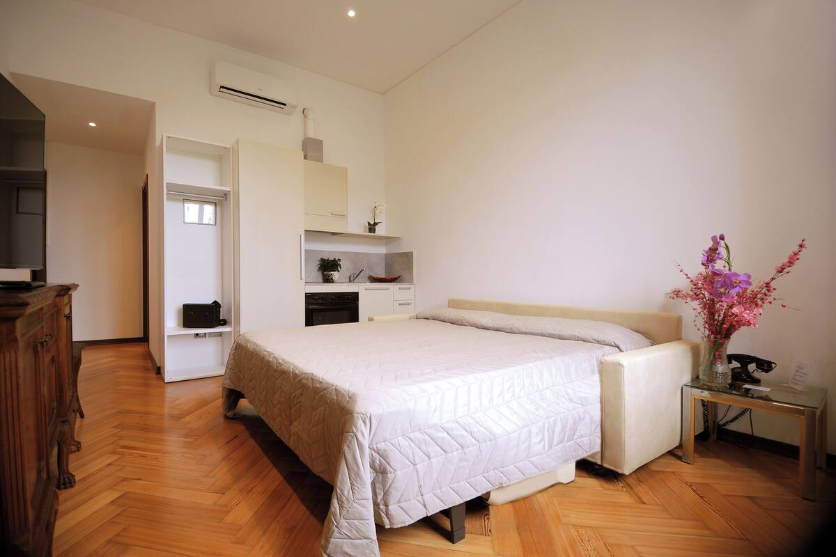 A bedroom with a bed, bedside table, and a small desk with a vase of flowers.