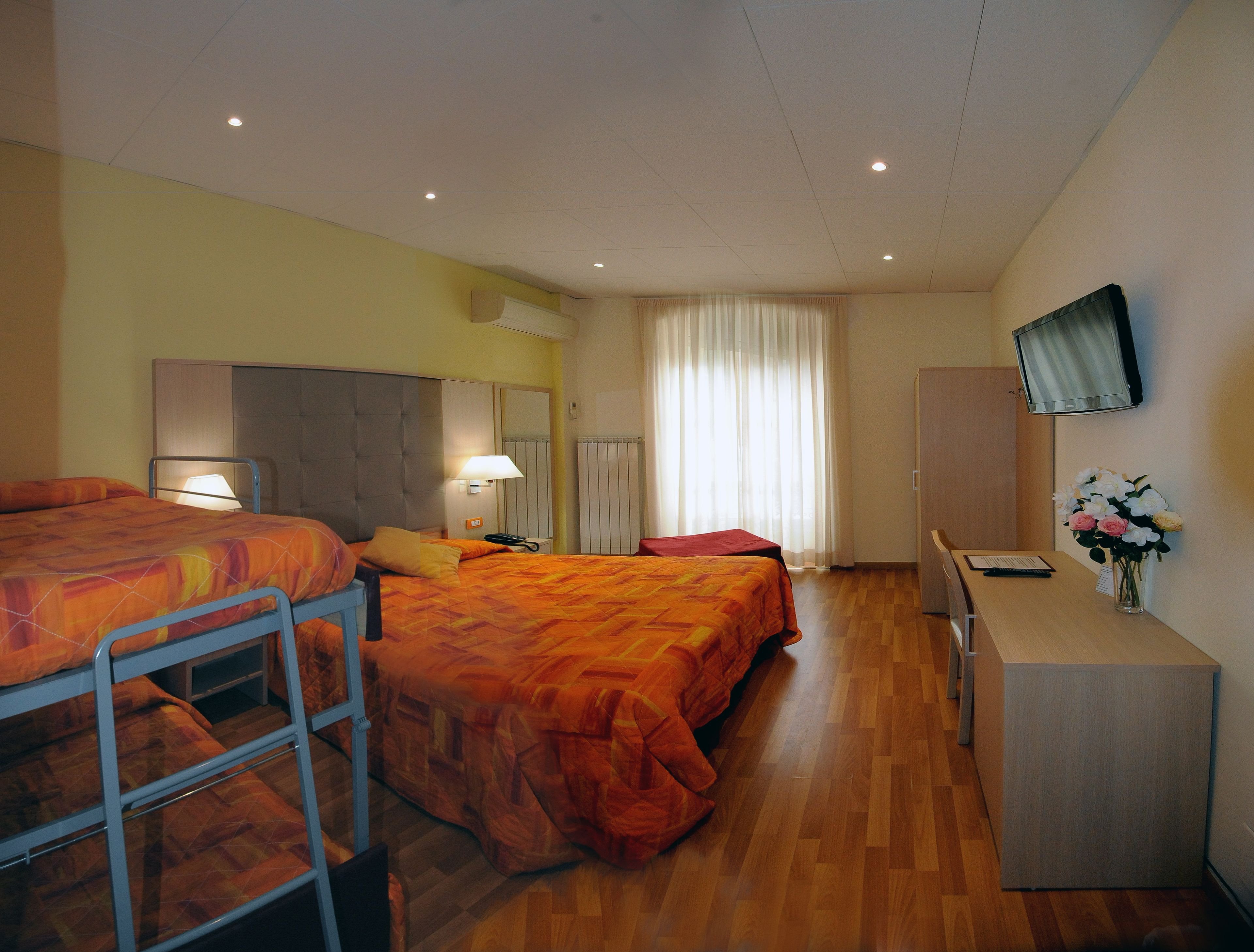 A hotel room with two beds, a desk, a TV, and a window with curtains.