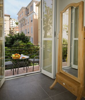 A balcony with a table set for dining, a wooden cabinet, and a view of neighboring buildings. - Hotel Alexander & Spa (Sanremo)