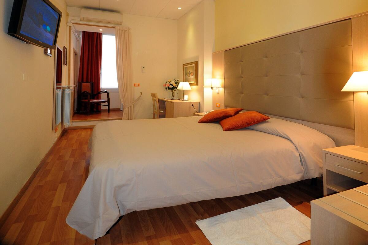 A hotel room with a large bed, bedside tables, a desk, and a television mounted on the wall.