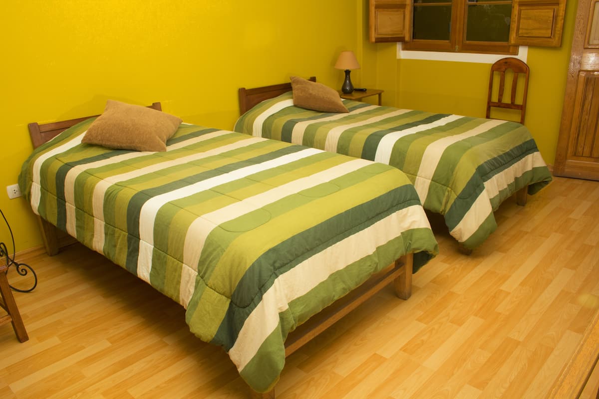 Deux lits simples avec une literie à rayures, des têtes de lit en bois et un plancher en bois, dans une pièce aux murs jaunes.