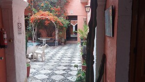A courtyard with a tiled floor, potted plants, a bench, and a cactus. - Posada Nueva España (Arequipa)