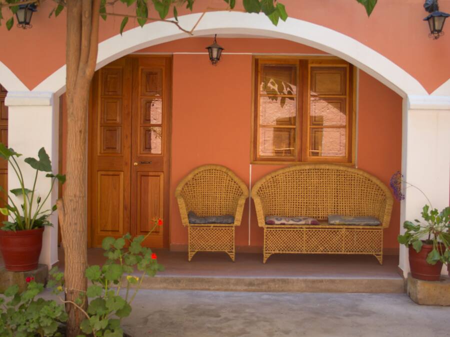 A building entrance with a porch, two wicker chairs, and potted plants.