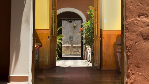 An open doorway leading to a courtyard with a hanging chandelier, a tiled floor, and a plant on the right. - Posada Nueva España (Arequipa)