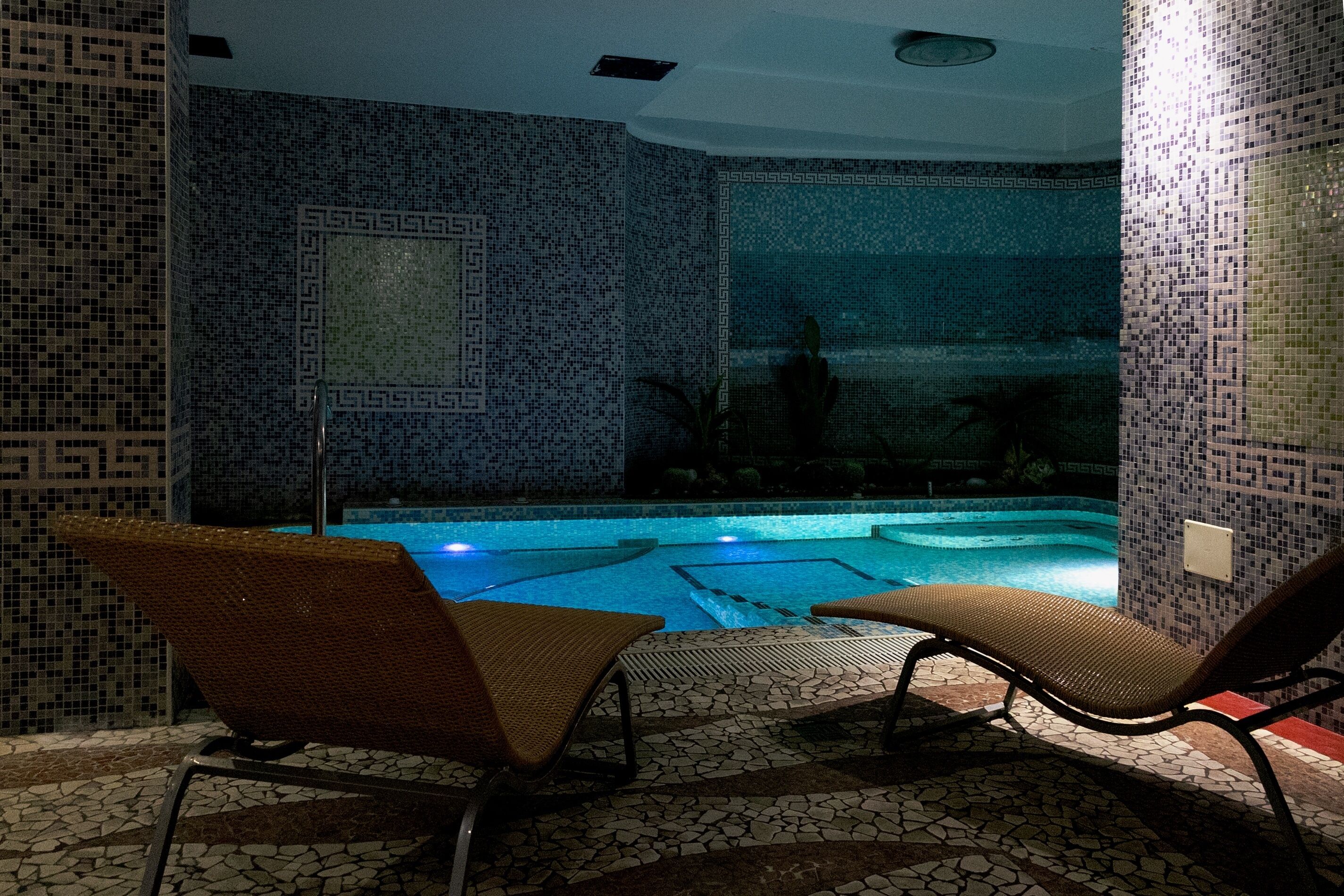 A pool area with mosaic tile walls and two lounge chairs facing the pool.