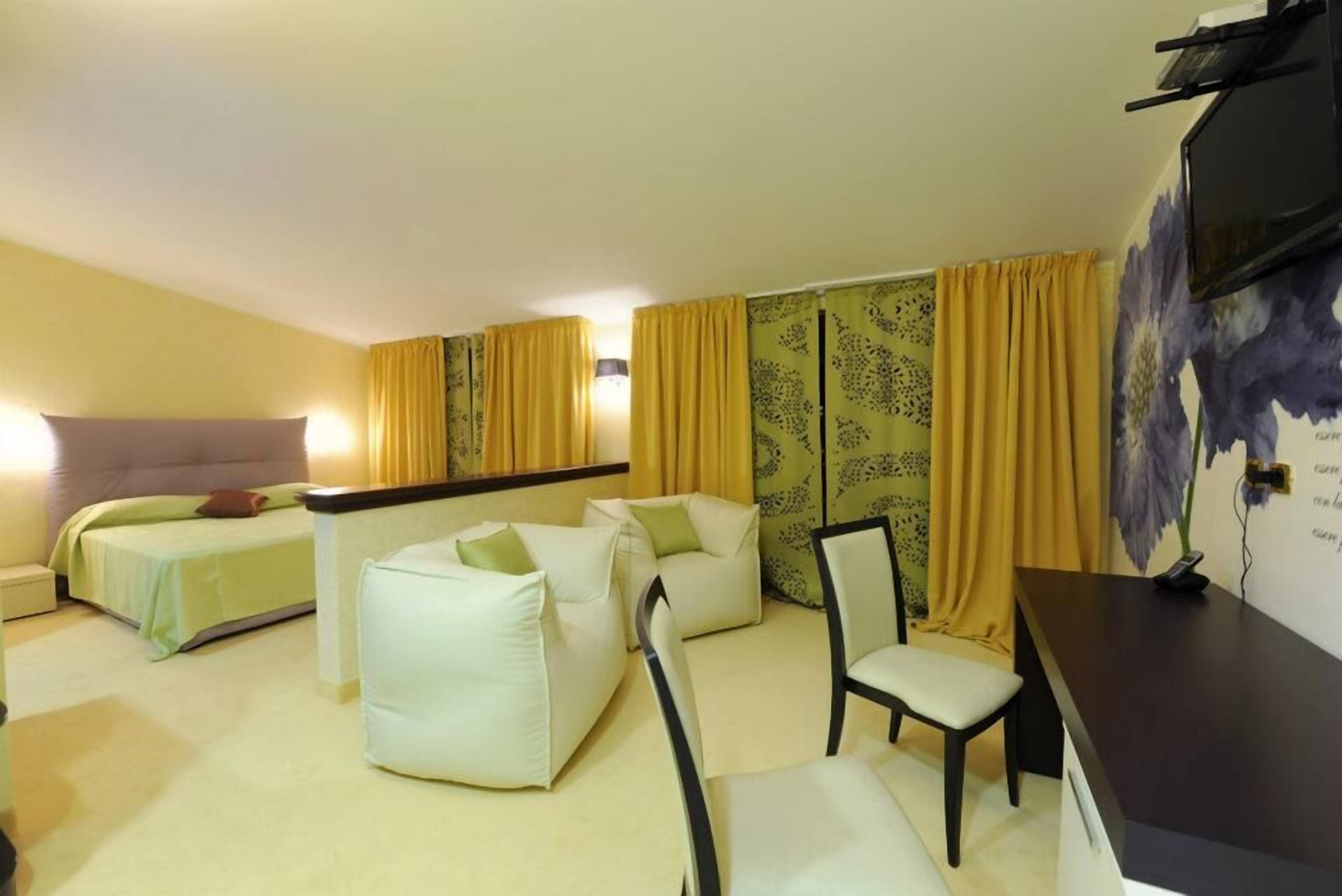 A hotel room with a bed, two sofas, a chair, a desk, and a TV.