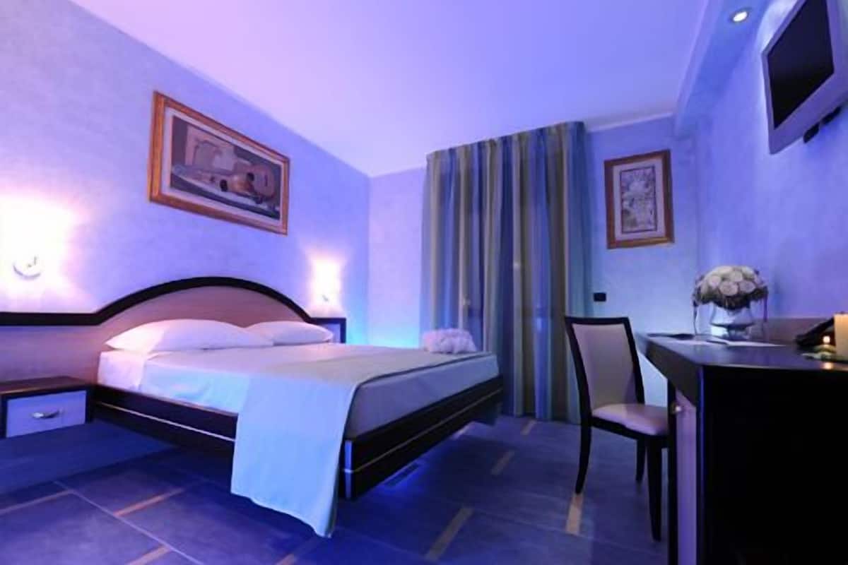 A hotel room with a bed, bedside table, chair, desk, and TV.
